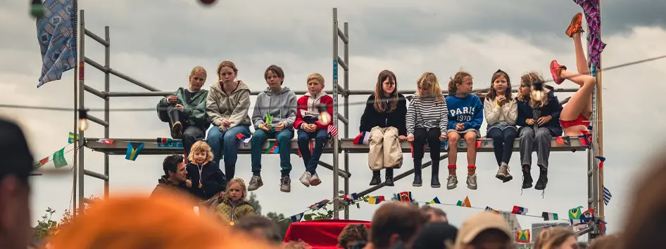Kinderen kijken toe vanaf een stelling naar de gebeurtenissen tijdens een dorpsfeest.